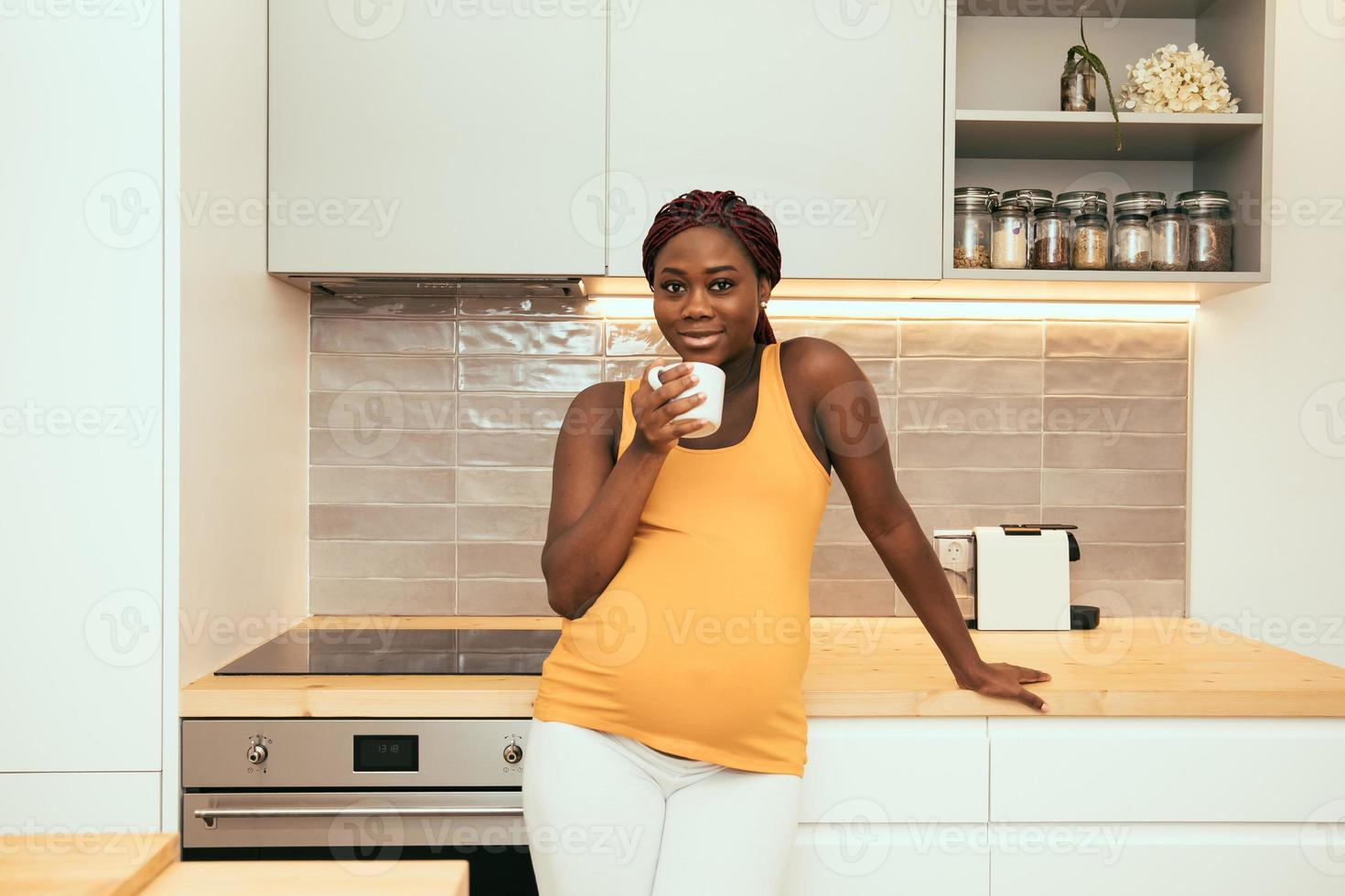 donna incinta nera che prende una tazza di caffè in cucina foto