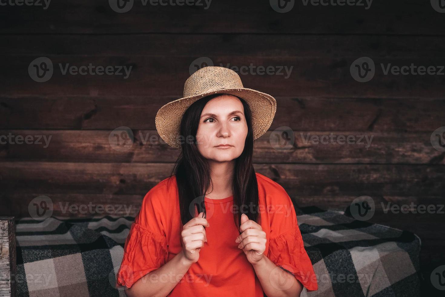 ritratto di una bella donna con un cappello di paglia vestito con abiti rossi sullo sfondo di una parete di legno foto