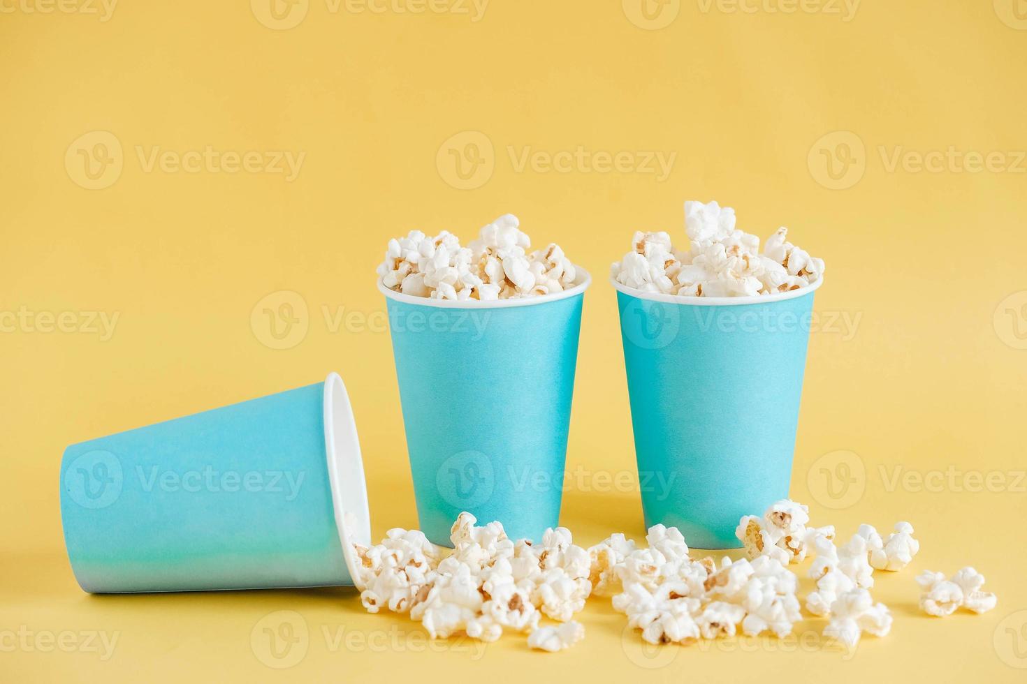 popcorn in bicchieri di carta blu su sfondo giallo. copia, spazio vuoto per il testo foto