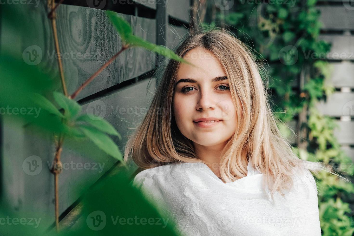 ritratto di una bella donna bionda in un verde lascia gli alberi su uno sfondo di parete in legno. copia, spazio vuoto per il testo foto