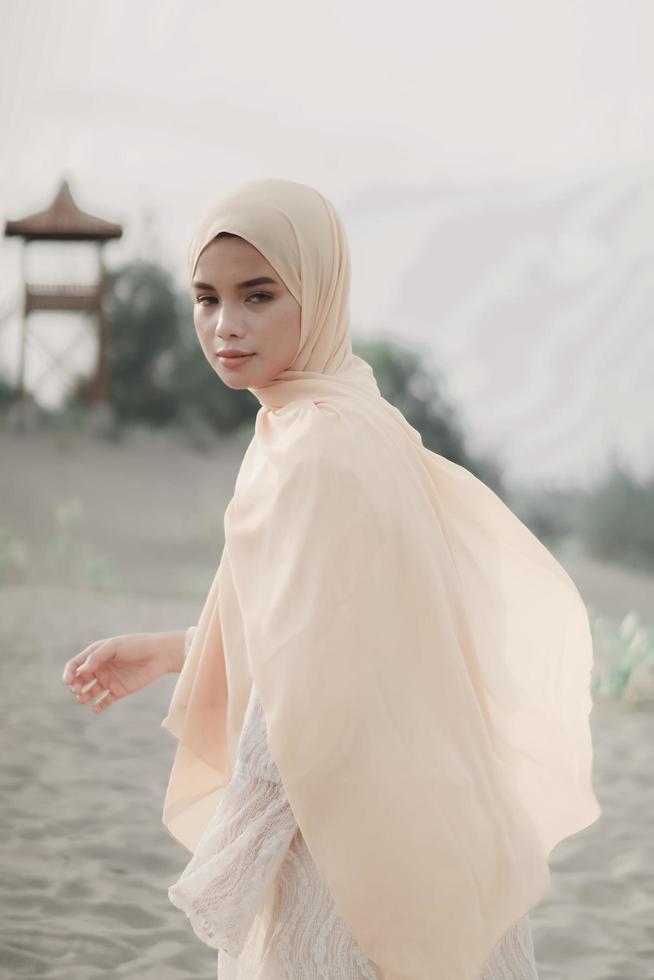 bella modella islamica che indossa la moda hijab, un moderno abito da sposa per donna musulmana cammina lungo la sabbia e il mare. una modella asiatica che usa l'hijab divertendosi in spiaggia. prematrimonio fotografico foto