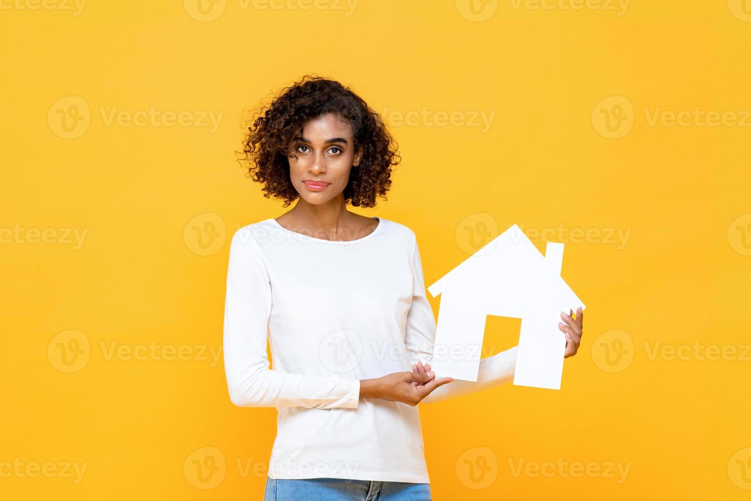 bella donna afroamericana che tiene ritaglio di casa isolato su sfondo giallo foto