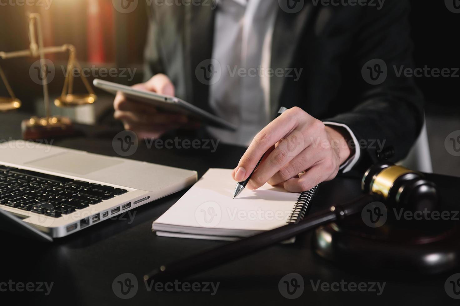 concetto di giustizia e diritto. giudice maschio in un'aula di tribunale il martelletto, lavorando con smartphone e laptop e computer tablet digitale foto