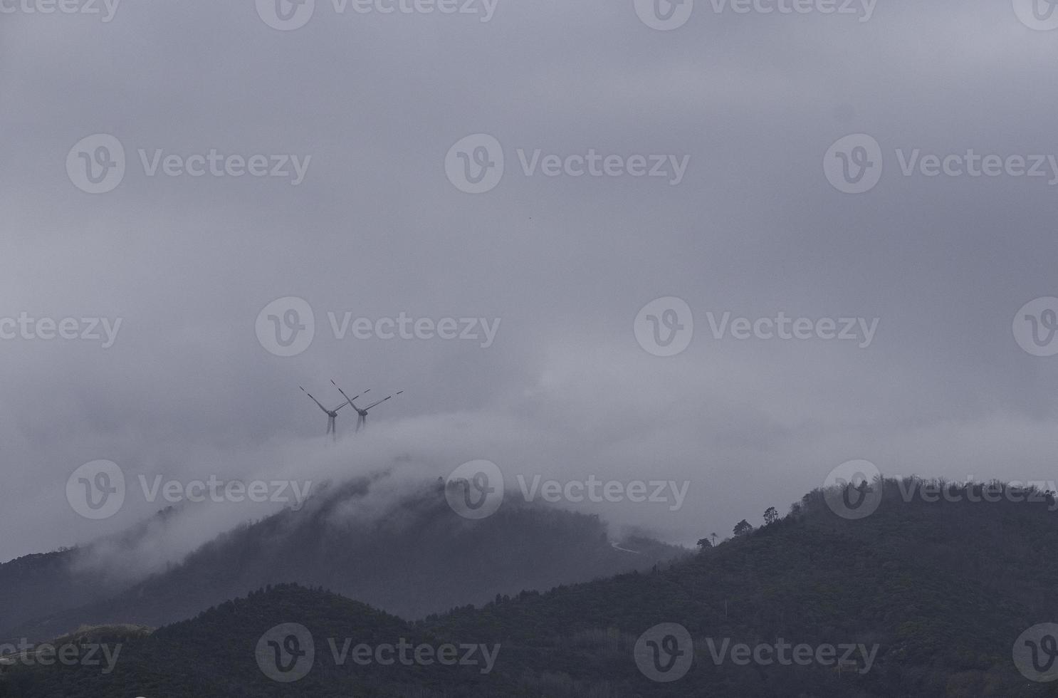 turbine eoliche che sfruttano l'energia del vento avvolte nella nebbia sulle colline costiere liguri foto