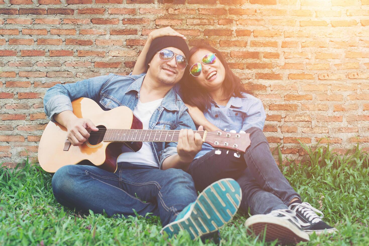 uomo hipster che suona la chitarra per la sua ragazza all'aperto contro un muro di mattoni, godendo insieme. foto