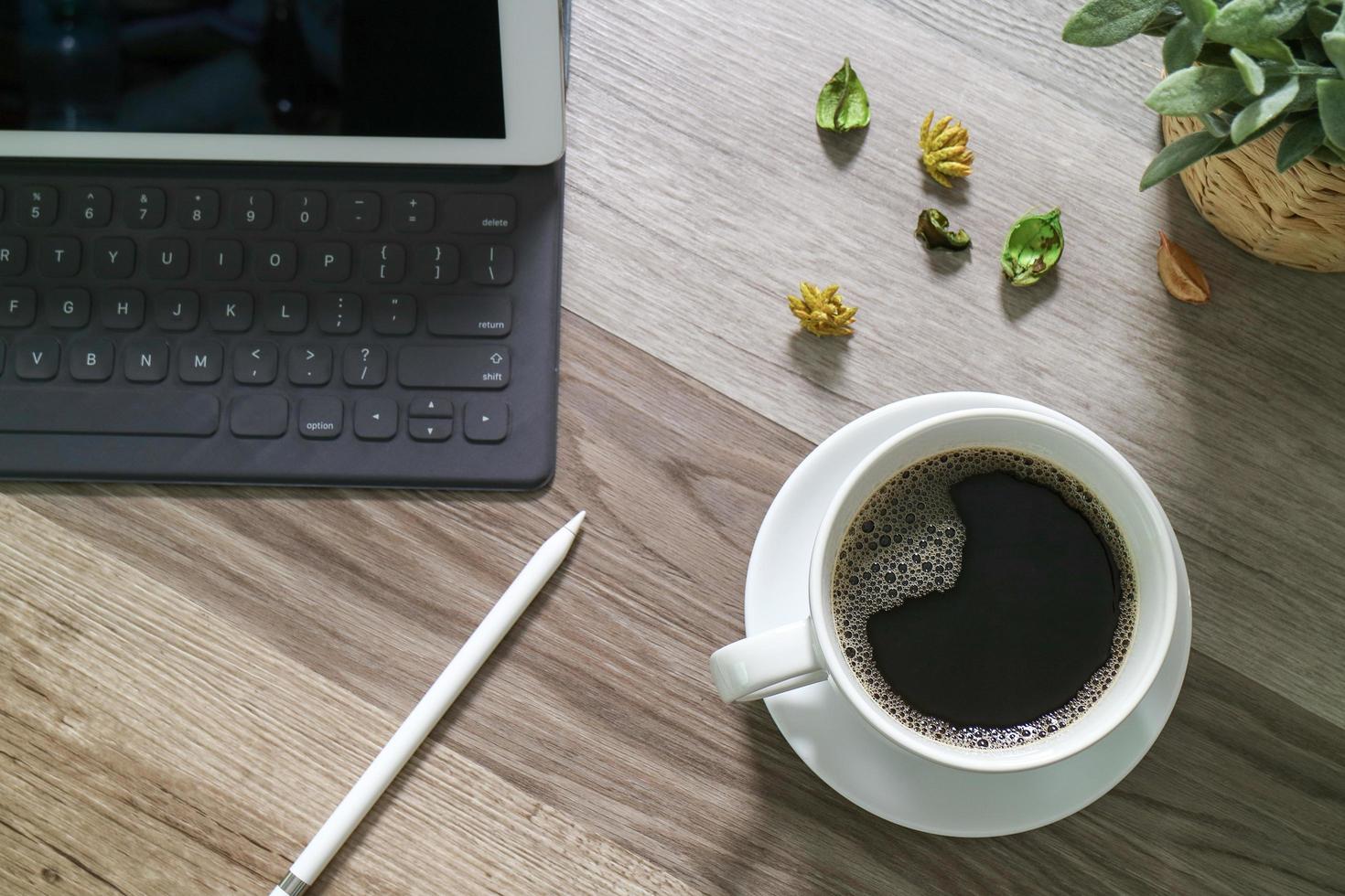 tazza di caffè e tastiera digitale dock da tavolo intelligente, vaso di erbe aromatiche, penna stilo sul tavolo di legno, effetto filtro foto