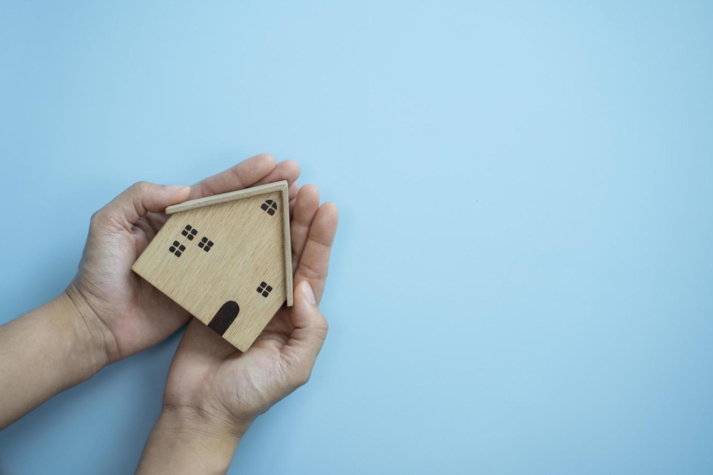 mani che tengono il legno della vecchia casa su sfondo blu pastello, concetto di assicurazione per la protezione della casa foto