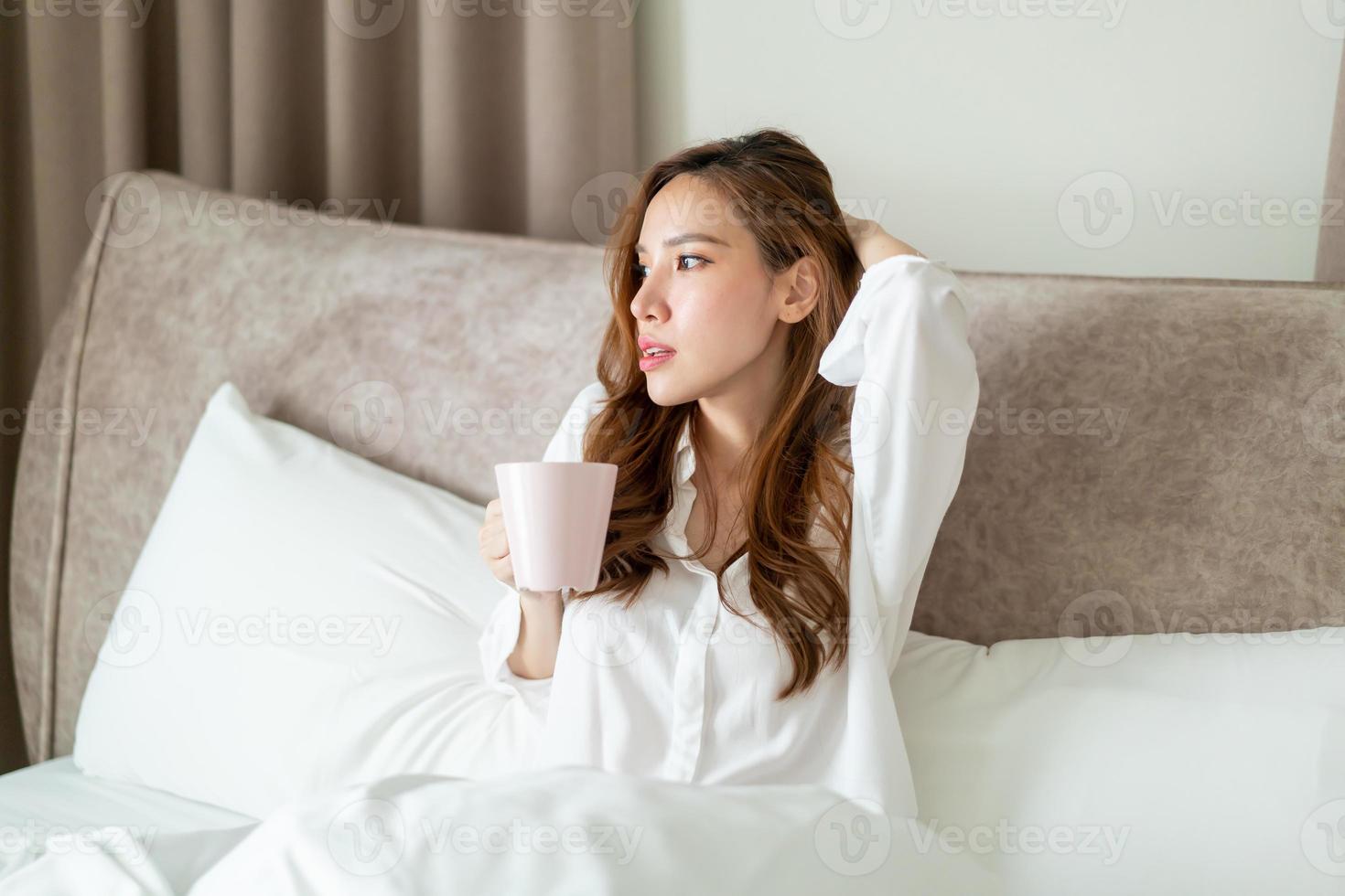 ritratto bella donna sveglia e tenendo tazza di caffè o tazza sul letto foto