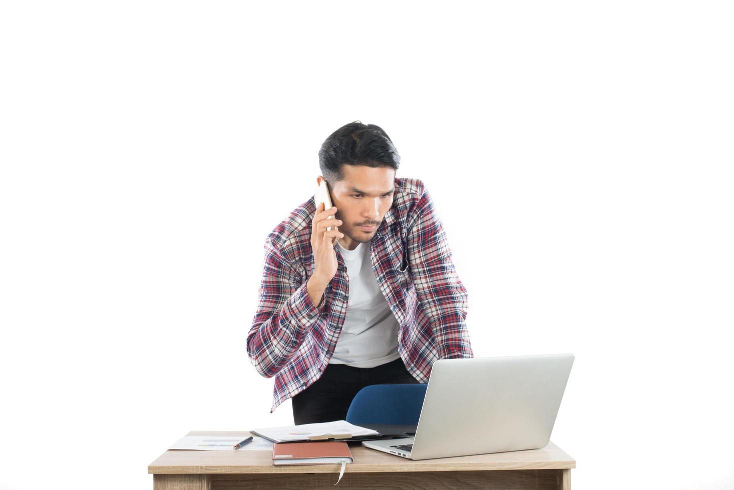 giovane uomo d'affari che parla al telefono mentre lavora al computer portatile in ufficio, tempo occupato con il lavoro isolato su priorità bassa bianca. foto