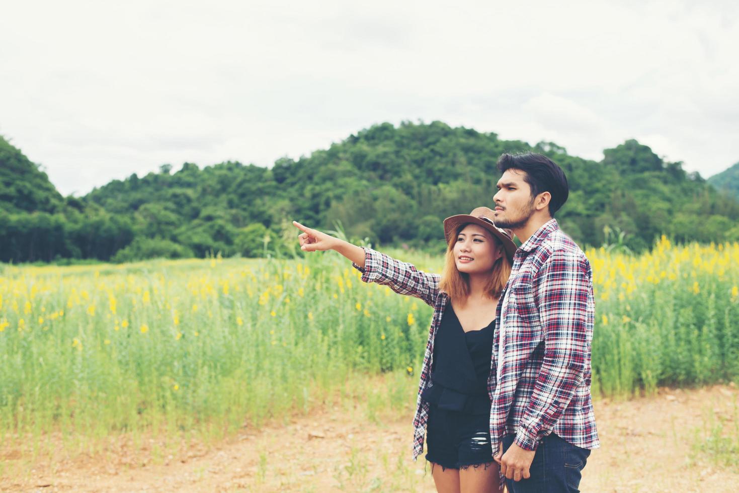 giovane coppia hipster fare una passeggiata attraverso i campi di fiori e indicò il cielo. il bel tempo è soleggiato. foto