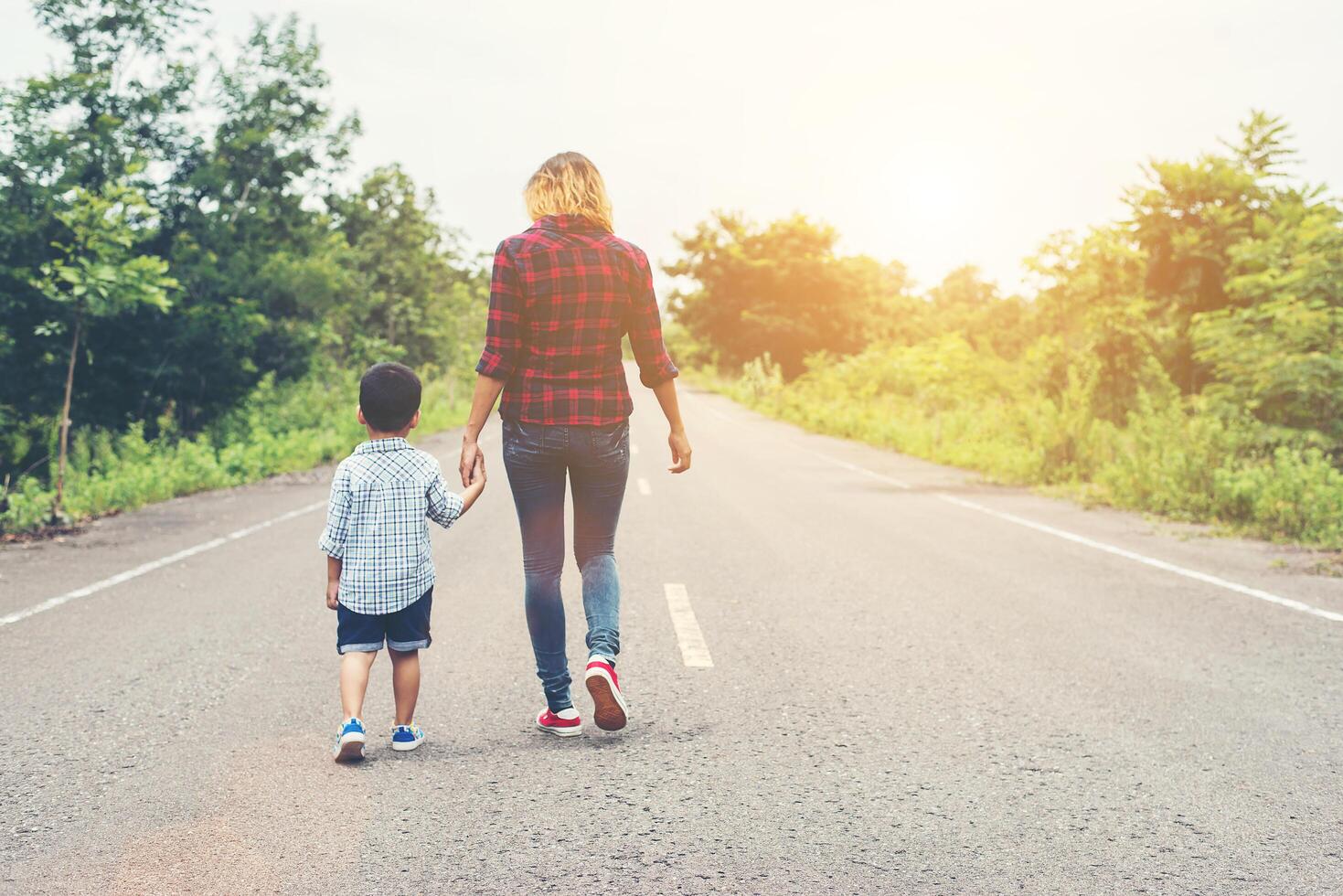 madre che tiene una mano di suo figlio in una giornata estiva che cammina per strada. foto