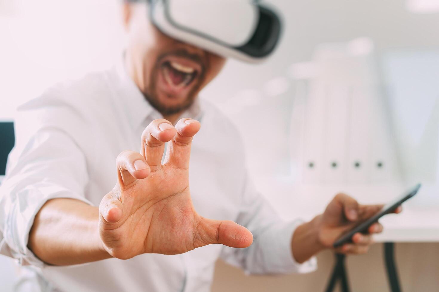 uomo d'affari che indossa occhiali per realtà virtuale in un ufficio moderno con telefono cellulare utilizzando con auricolare vr foto