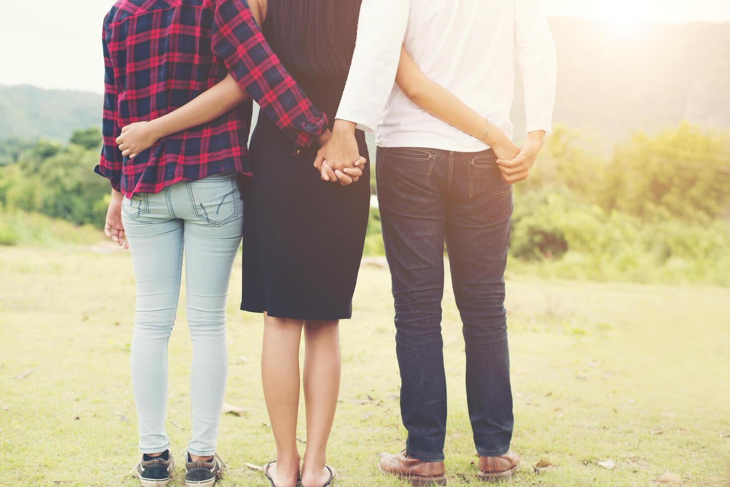 triangolo amoroso, l'uomo sta abbracciando una donna e si tiene per mano con un'altra ragazza, in piedi all'aperto nel parco. foto