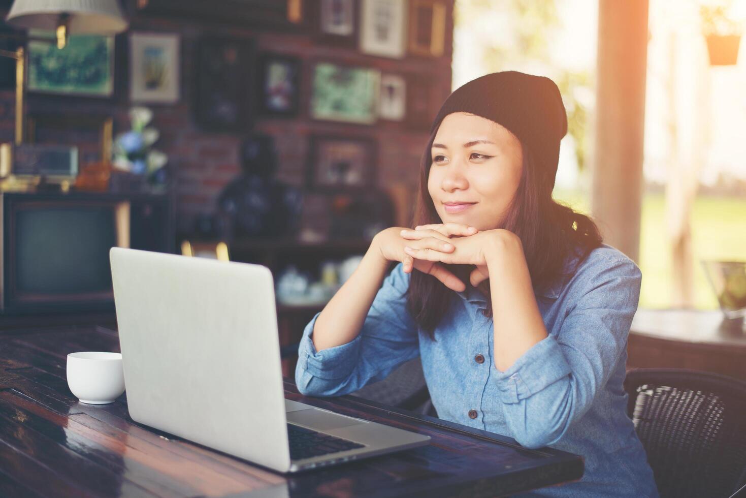 bella giovane donna hipster seduta in una caffetteria, rilassarsi e giocare con il suo computer portatile, trovare informazioni sul tempo libero, felice e divertente. concetto di stile di vita. foto