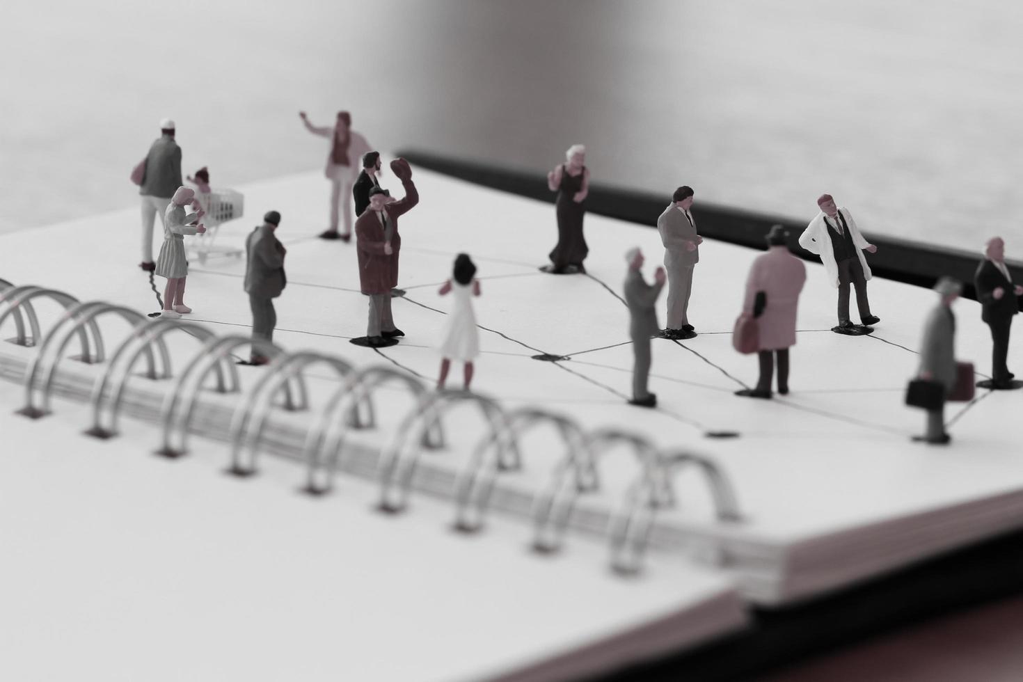 primo piano di persone in miniatura con diagramma di rete sociale su taccuino aperto su scrivania in legno come concetto di social media foto