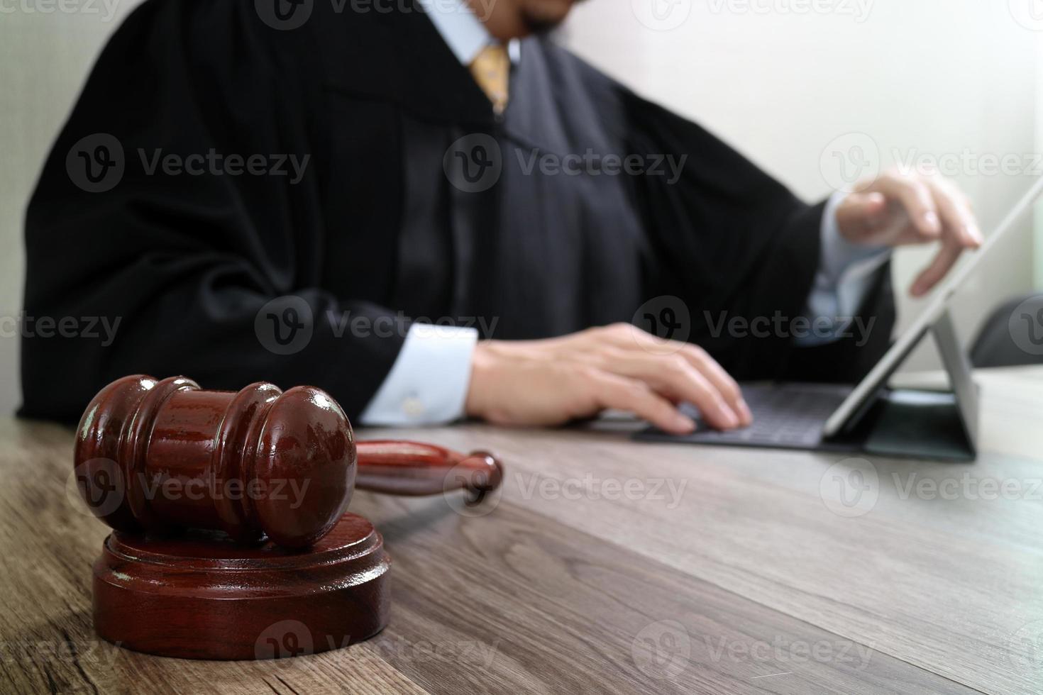 concetto di giustizia e diritto. giudice maschio in un'aula di tribunale con il martelletto, lavorando con la tastiera di aggancio del computer tablet digitale su un tavolo di legno foto