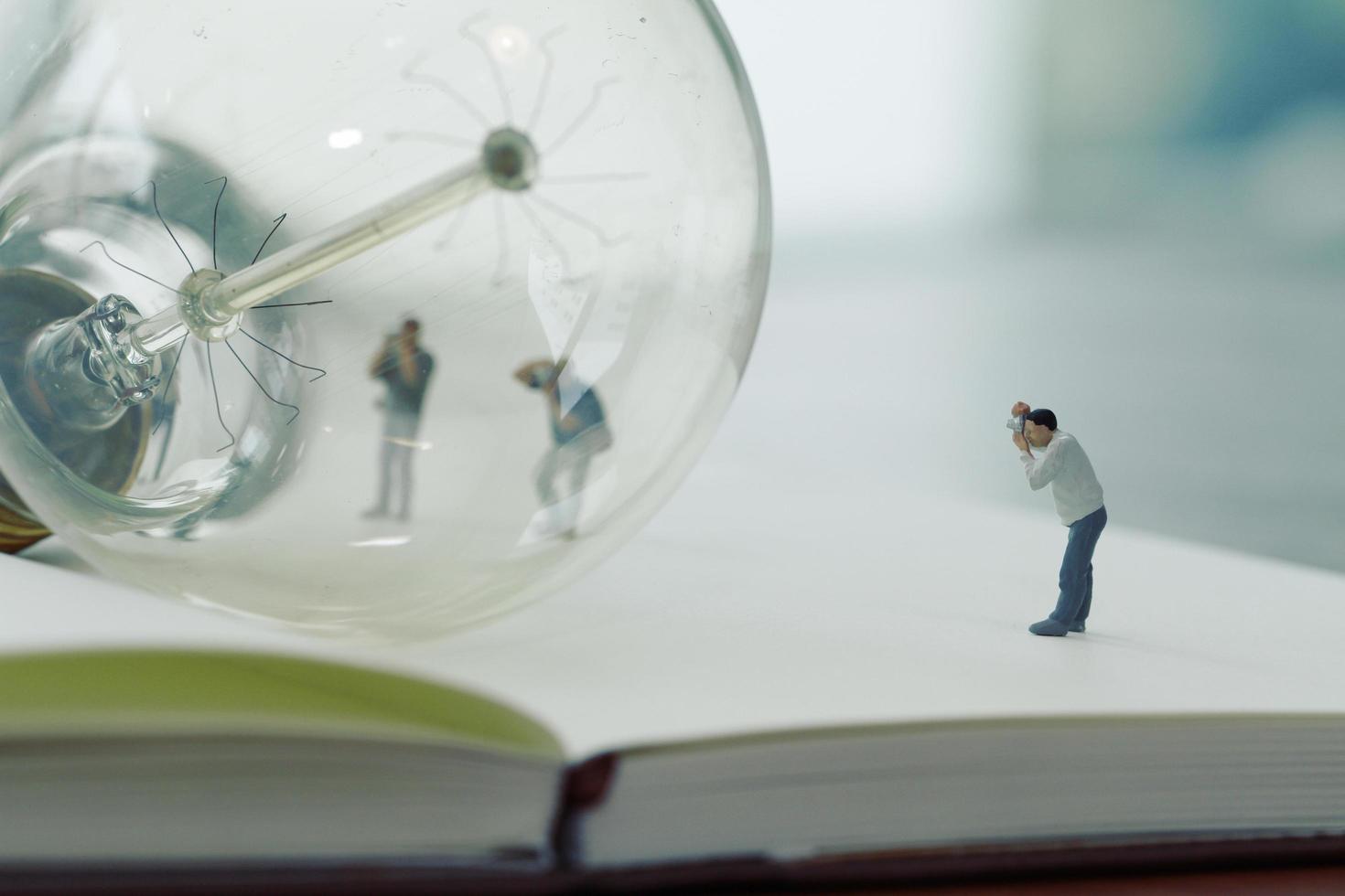 concetto di idea creativa - fotografo in miniatura con lampadina vintage su quaderno di carta aperto foto