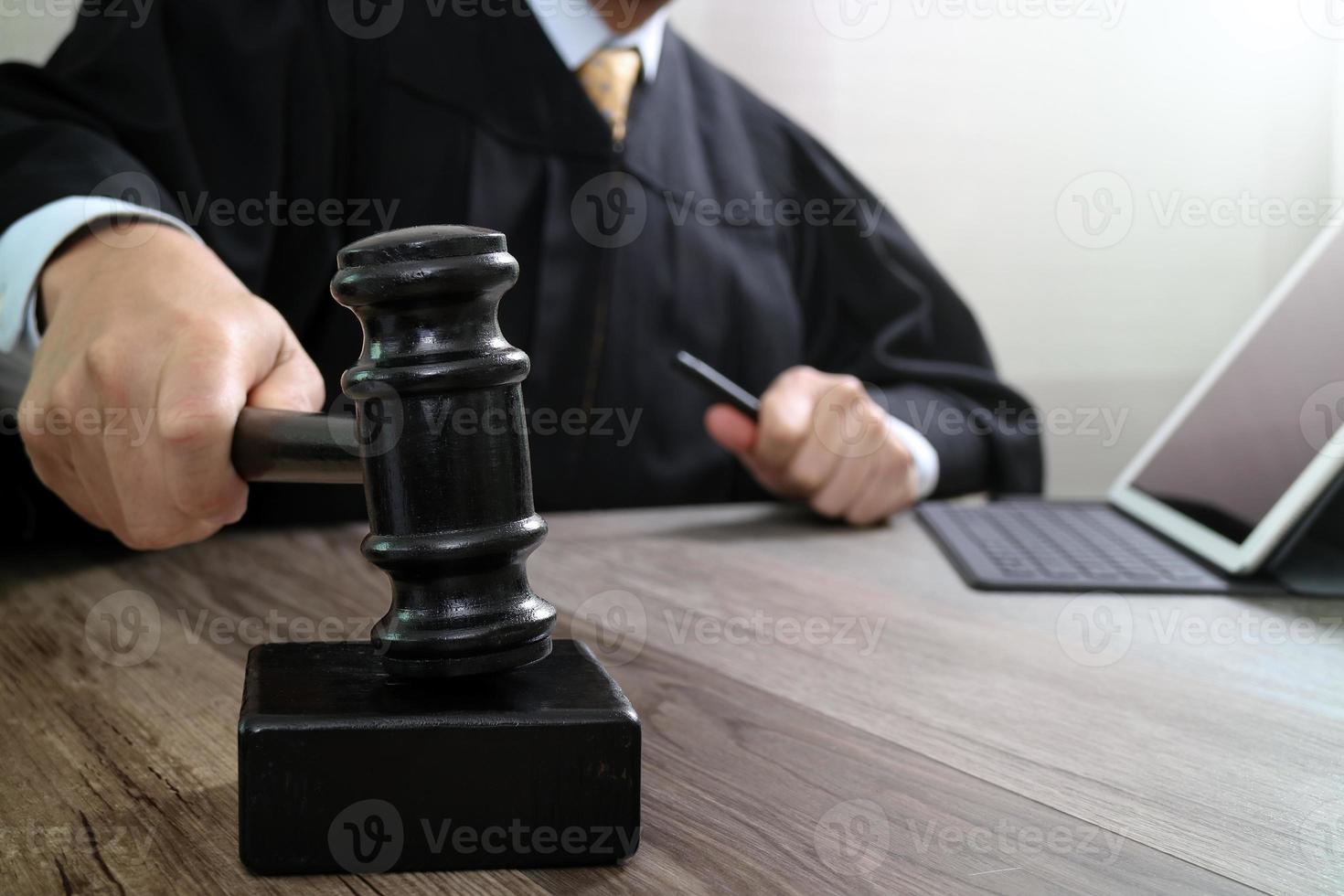concetto di giustizia e diritto. giudice maschio in un'aula di tribunale che colpisce il martelletto, lavorando con la tastiera di aggancio del computer tablet digitale su un tavolo di legno foto
