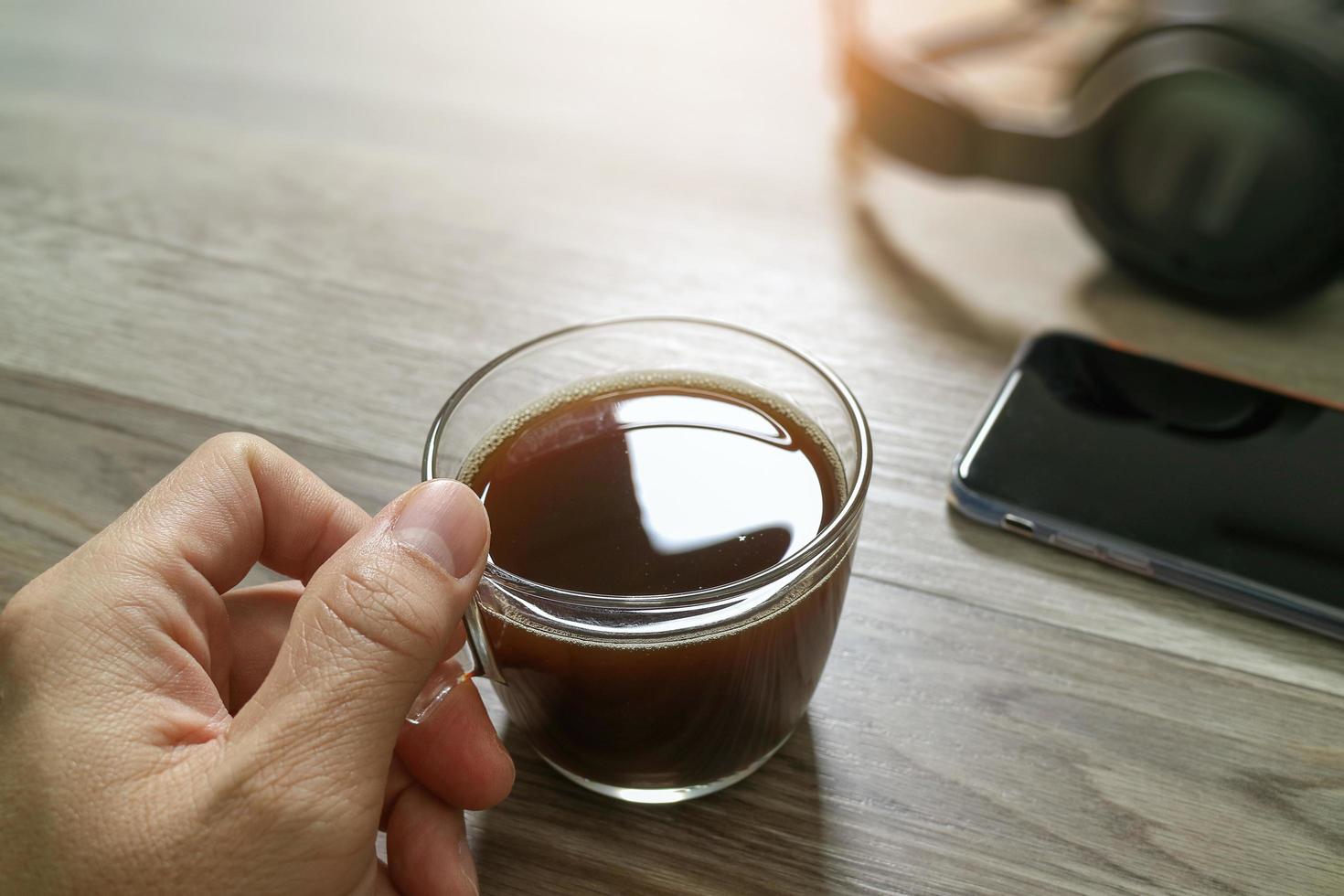 mano che tiene tazza di caffè o auricolare per tè e voip, smartphone sul tavolo di legno, effetto filtro foto