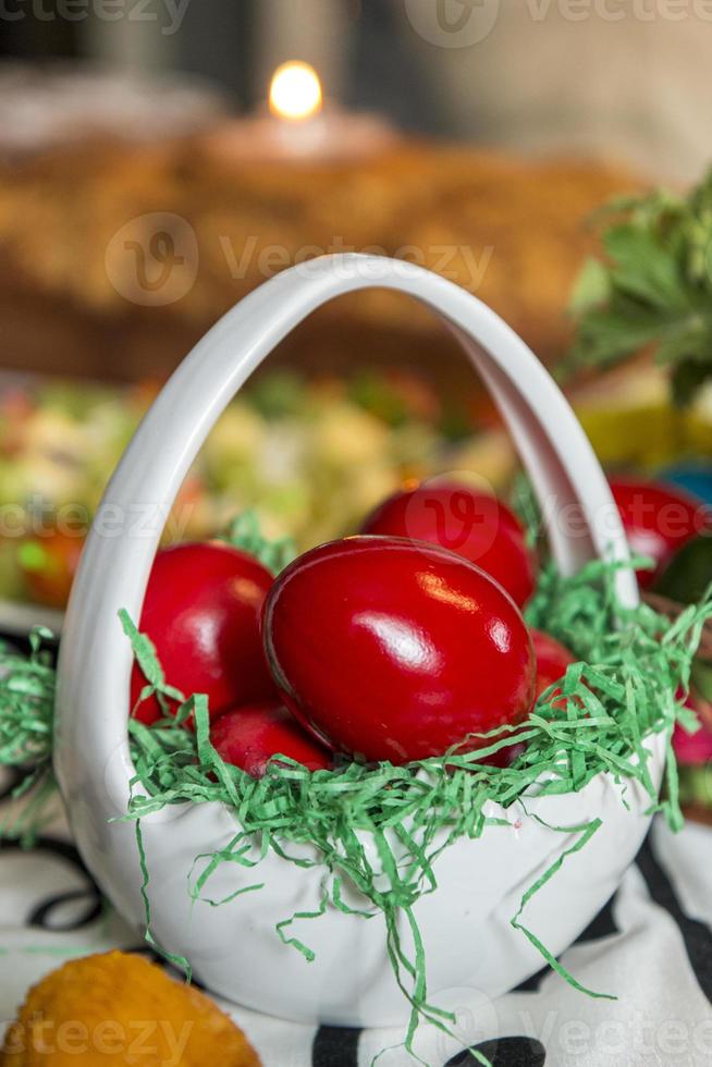 tavola di Pasqua con uova colorate di rosso, pane, rami verdi decorati, su tavola di legno bianco tavolato con tovaglia in tessuto. foto