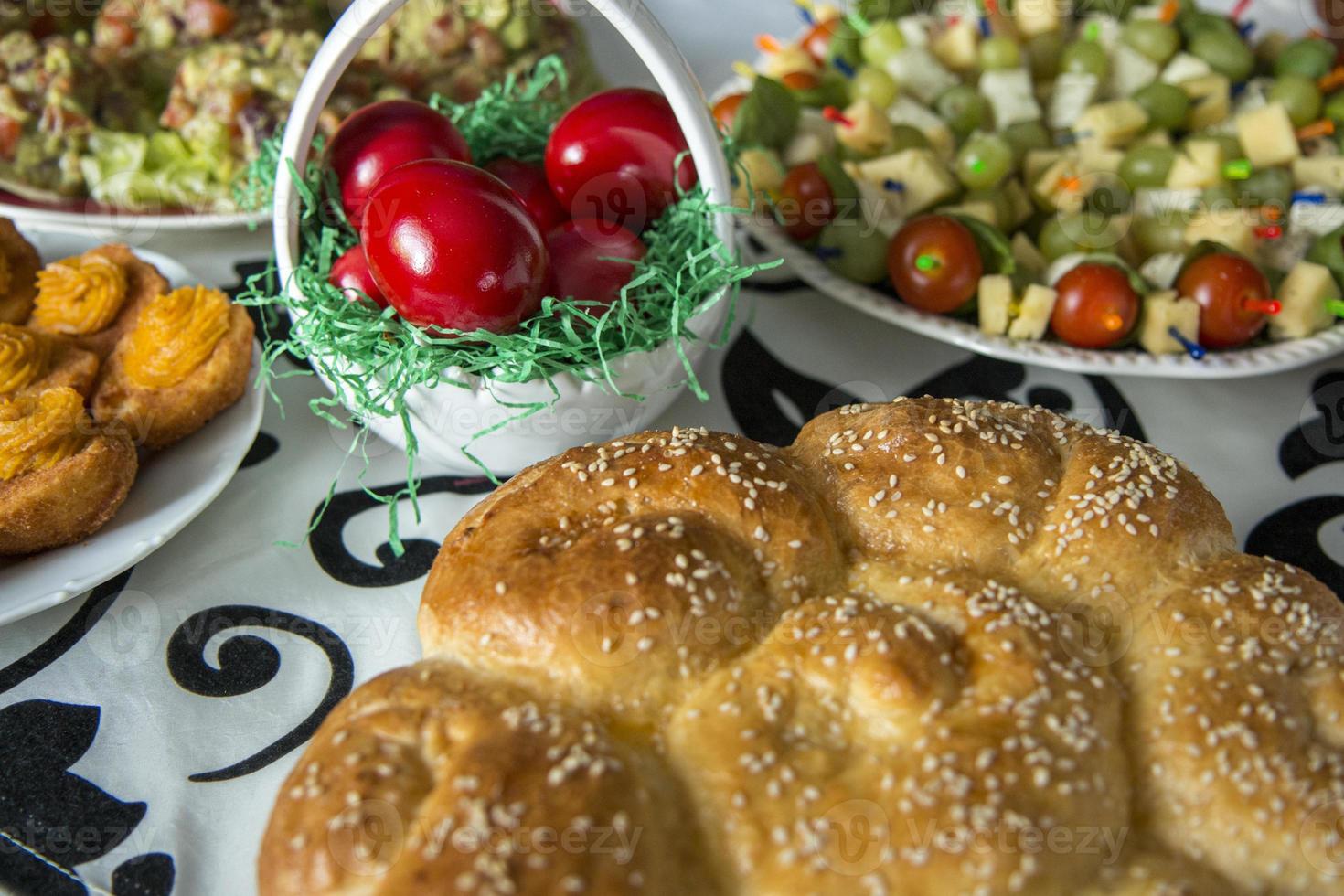 tavola di Pasqua con uova colorate di rosso, pane, rami verdi decorati, su tavola di legno bianco tavolato con tovaglia in tessuto. foto