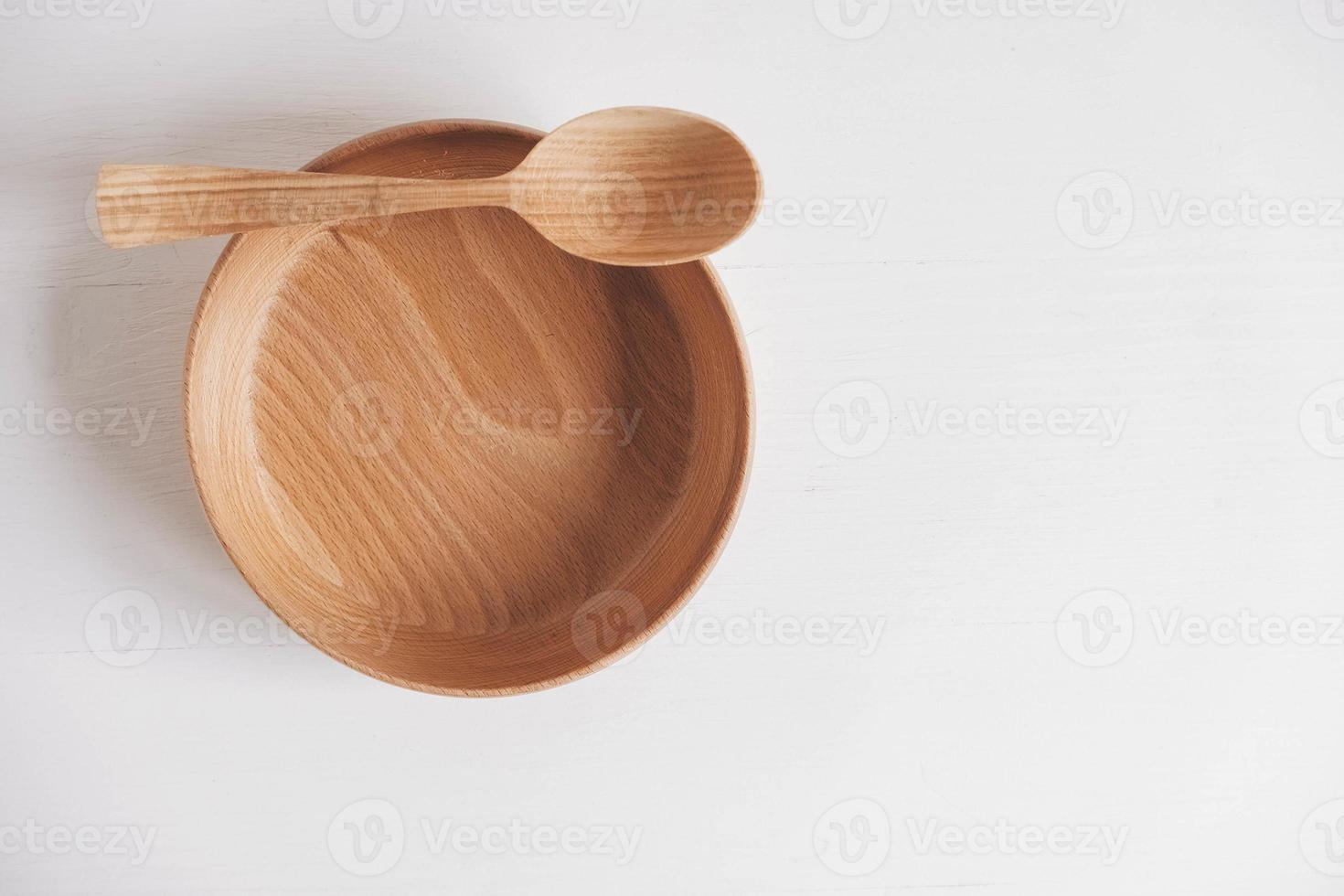 ciotola di legno vuota e cucchiaio di legno su uno sfondo bianco da tavola. vista dall'alto. copia, spazio vuoto per il testo foto
