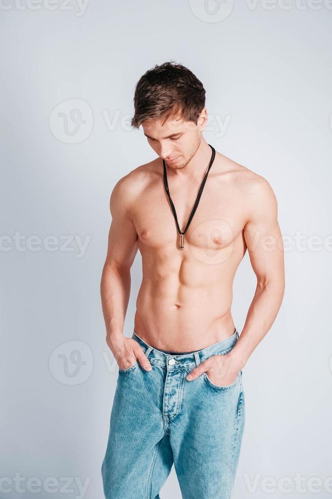 giovane uomo muscoloso con un torso nudo vestito in blue jeans su sfondo bianco foto