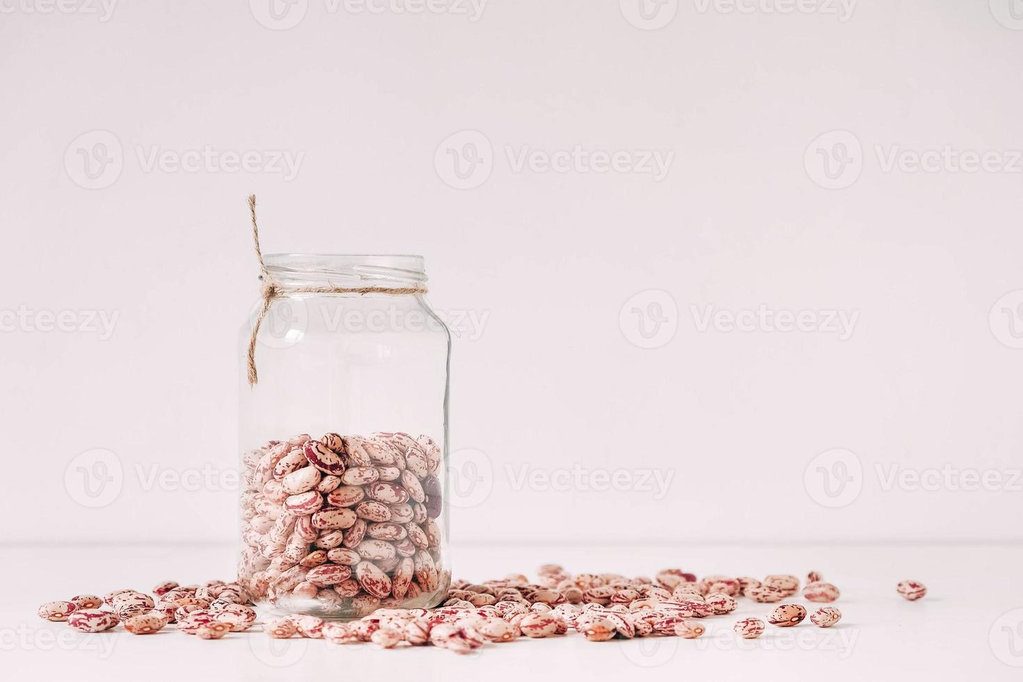 fagioli secchi in un barattolo di vetro sparsi su uno sfondo bianco da tavola. copia, spazio vuoto per il testo foto