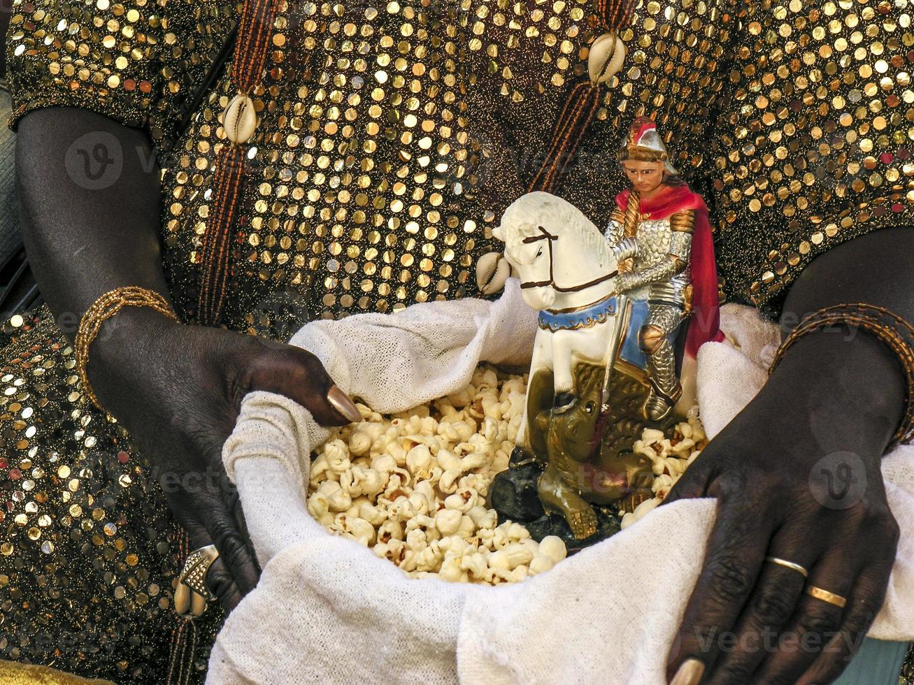 Madre di santo candomble tiene un cesto con popcorn e l'immagine di san giorgio ogum davanti alla chiesa foto