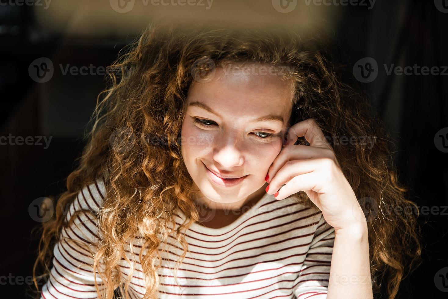 giovane donna piuttosto caucasica positiva che sorride e pensa con la mano che tocca il viso al mattino presto foto