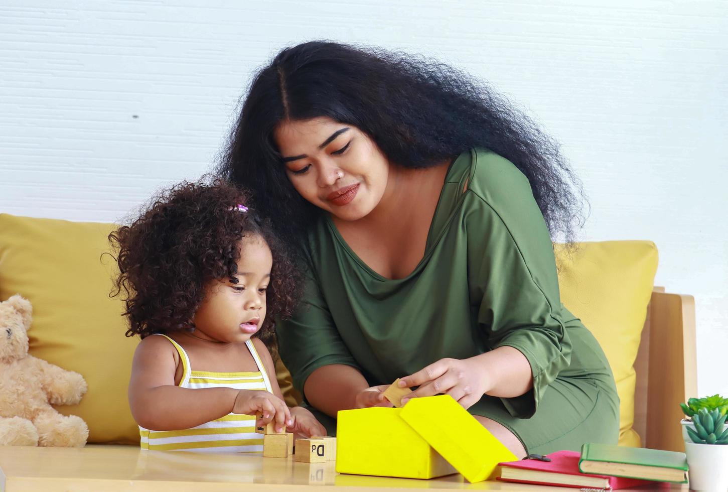 la madre si diverte a giocare con la figlia in vacanza e le scatole regalo gialle la figlia dai capelli ricci gioca con la madre in casa. foto