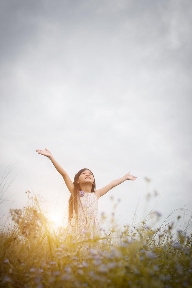 piccola ragazza asiatica carina in piedi tra il giorno del sole del campo di fiori viola. libertà godendo con la natura. foto