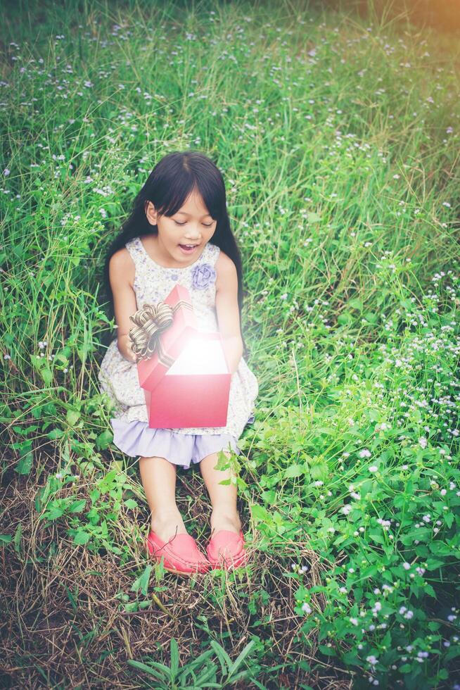 bambina seduta vicino al campo con un regalo e guardandolo così sorpresa foto