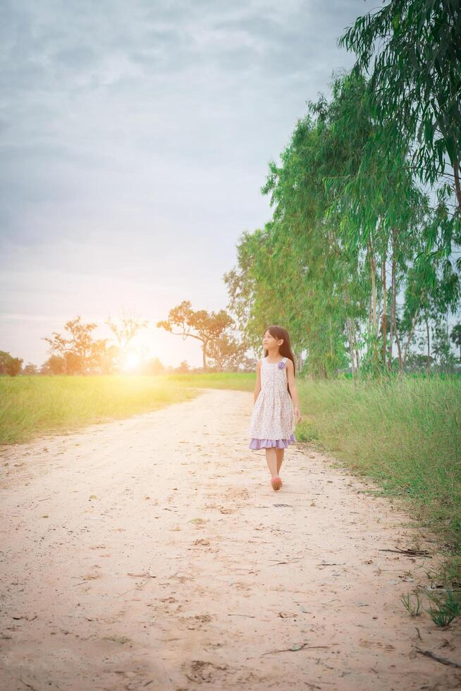 la bambina che indossa un vestito sta camminando e distoglie lo sguardo dalla strada rurale. foto
