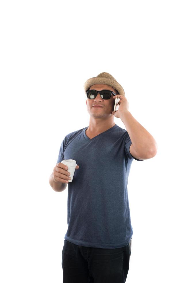 bel hipster giovane in cappello e occhiali da sole in piedi e parlando al cellulare su sfondo bianco. foto