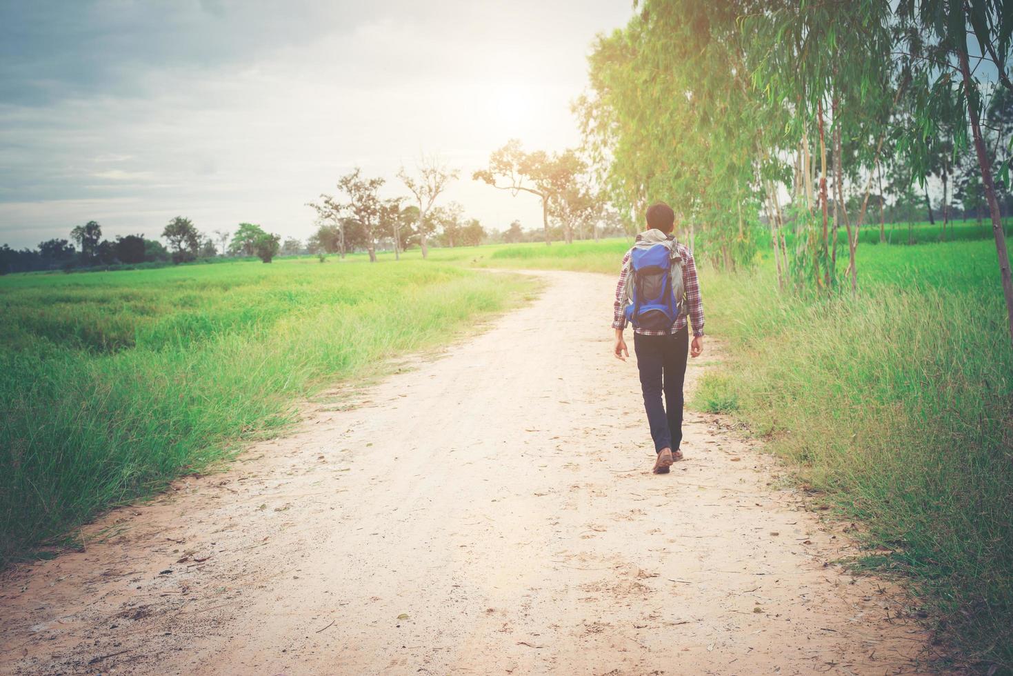 parte posteriore di un giovane hipster con zaino in spalla che cammina per la campagna. foto