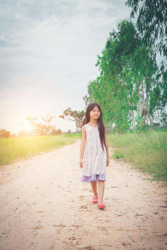 la bambina con i capelli lunghi che indossa un vestito si sta allontanando da te lungo una strada rurale. foto