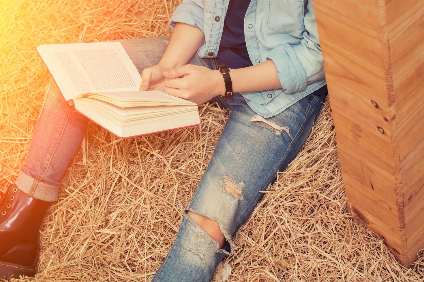 giovane uomo che legge un libro e seduto sulla paglia nella fattoria foto