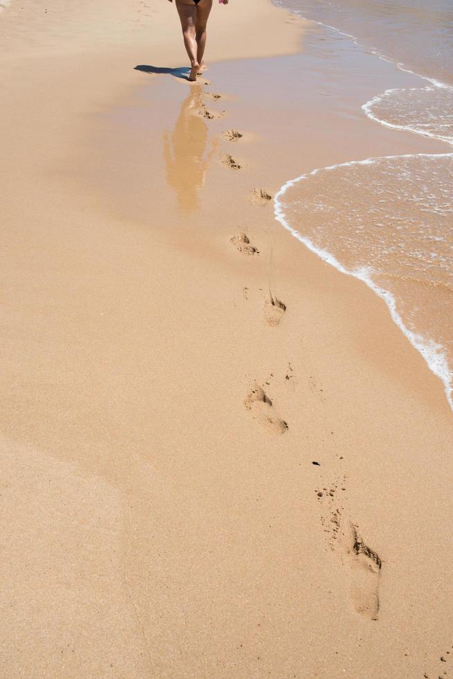 donna caucasica vista dalla schiena che cammina su una spiaggia deserta. Impronte nella sabbia. sistema circolatorio è migliorato dall'esercizio aerobico, come camminare in riva al mare. Portogallo foto