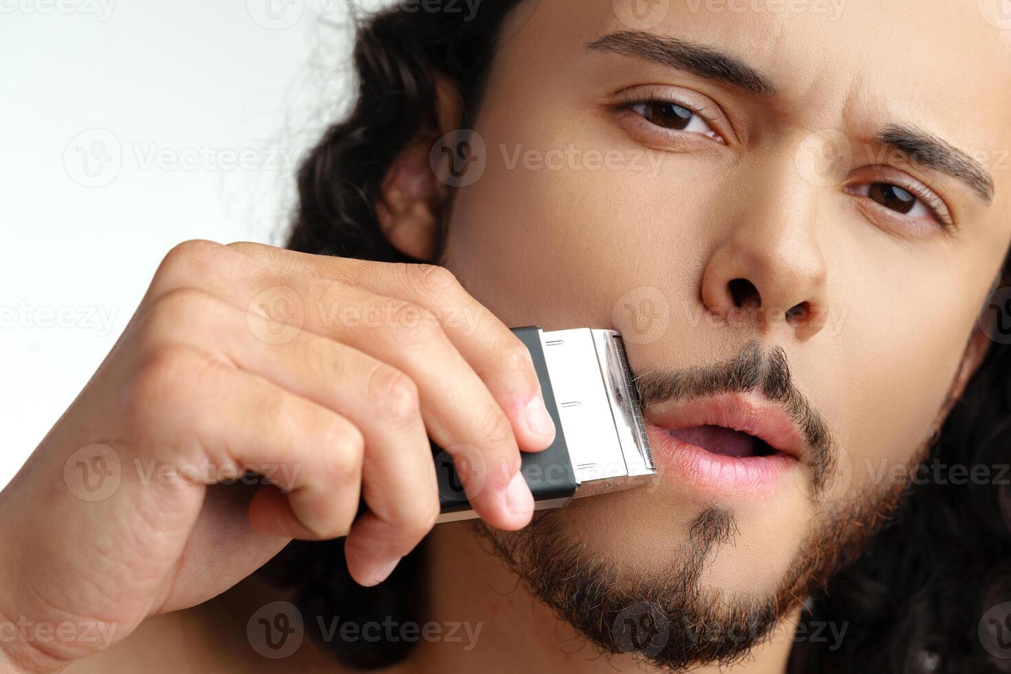 uomo Rifinitura il suo barba in casa utilizzando un elettrico trimmer mentre in mostra il suo personale governare routine foto