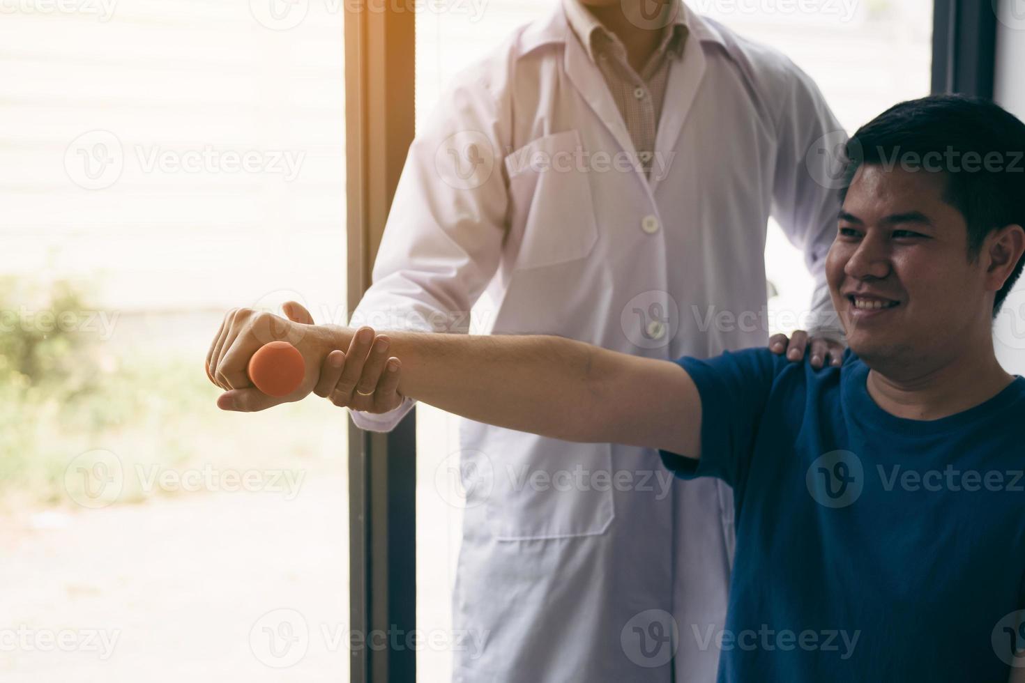 fisioterapista asiatico che aiuta un paziente che solleva i manubri a lavorare durante il suo recupero con i pesi nella stanza della clinica. foto