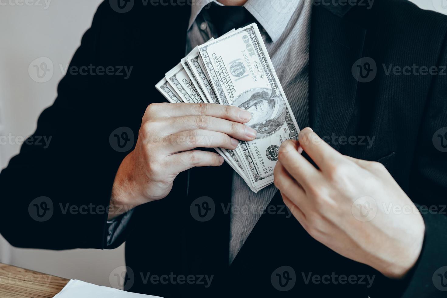 uomo d'affari che mette una pila di banconote nella tasca del cappotto del vestito. foto