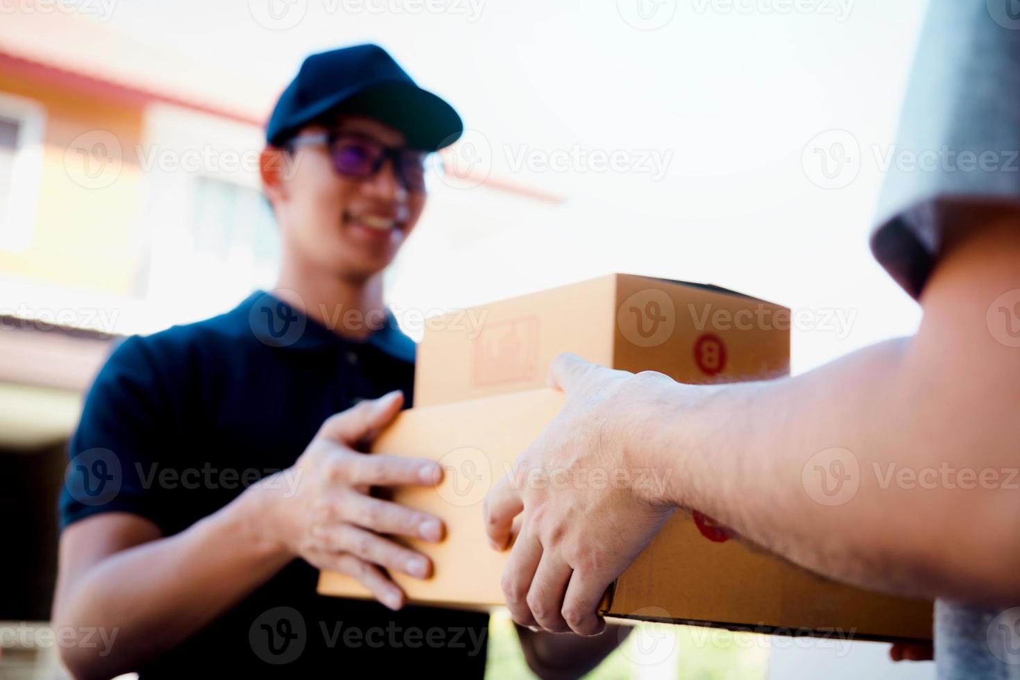 il corriere asiatico tiene una scatola di cartone con il pacco all'interno e il destinatario sta firmando il pacco. foto