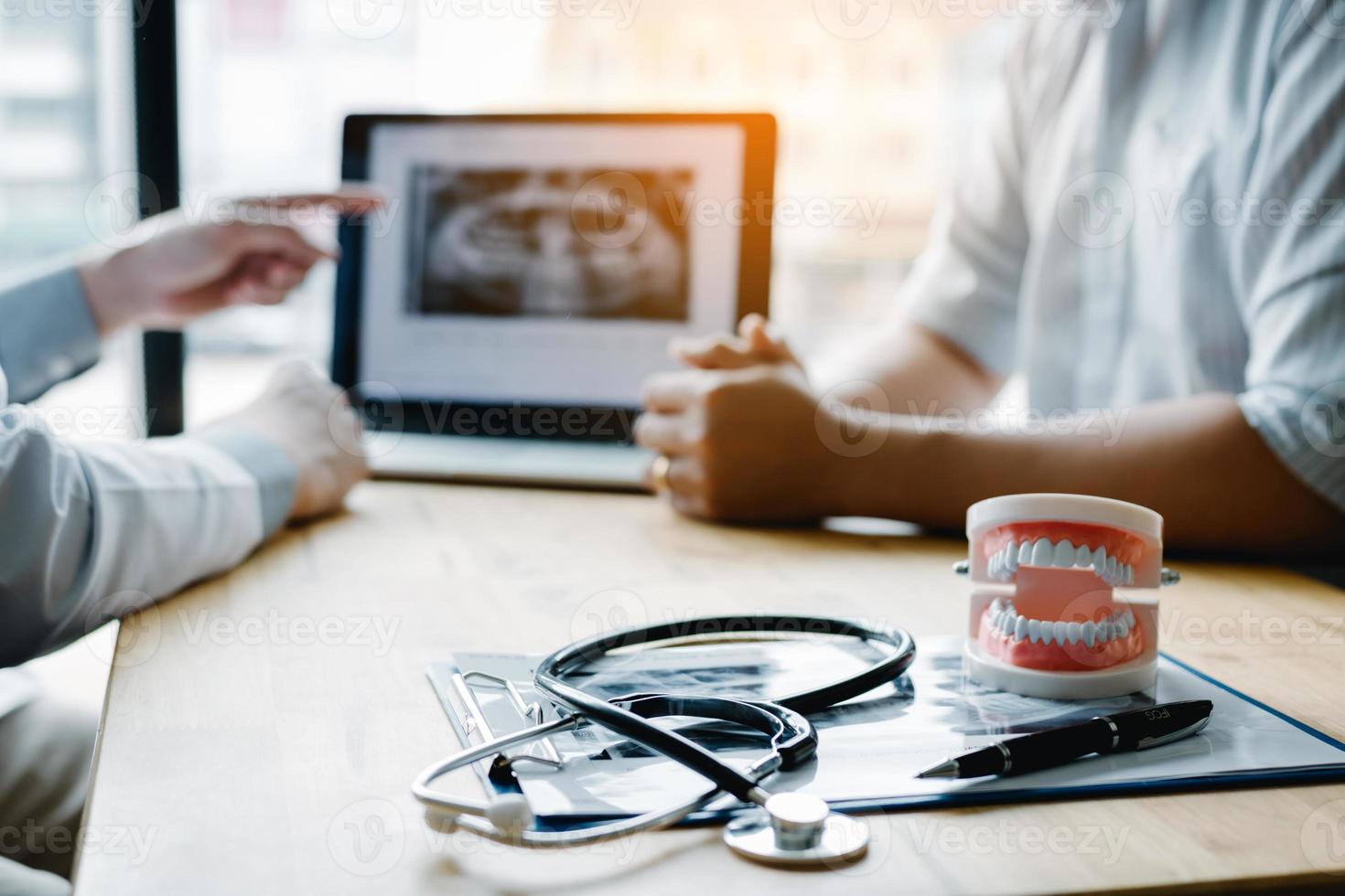 mano del dentista che punta l'immagine a raggi X nel computer portatile e parla con il paziente di trattamenti farmacologici e chirurgici. foto