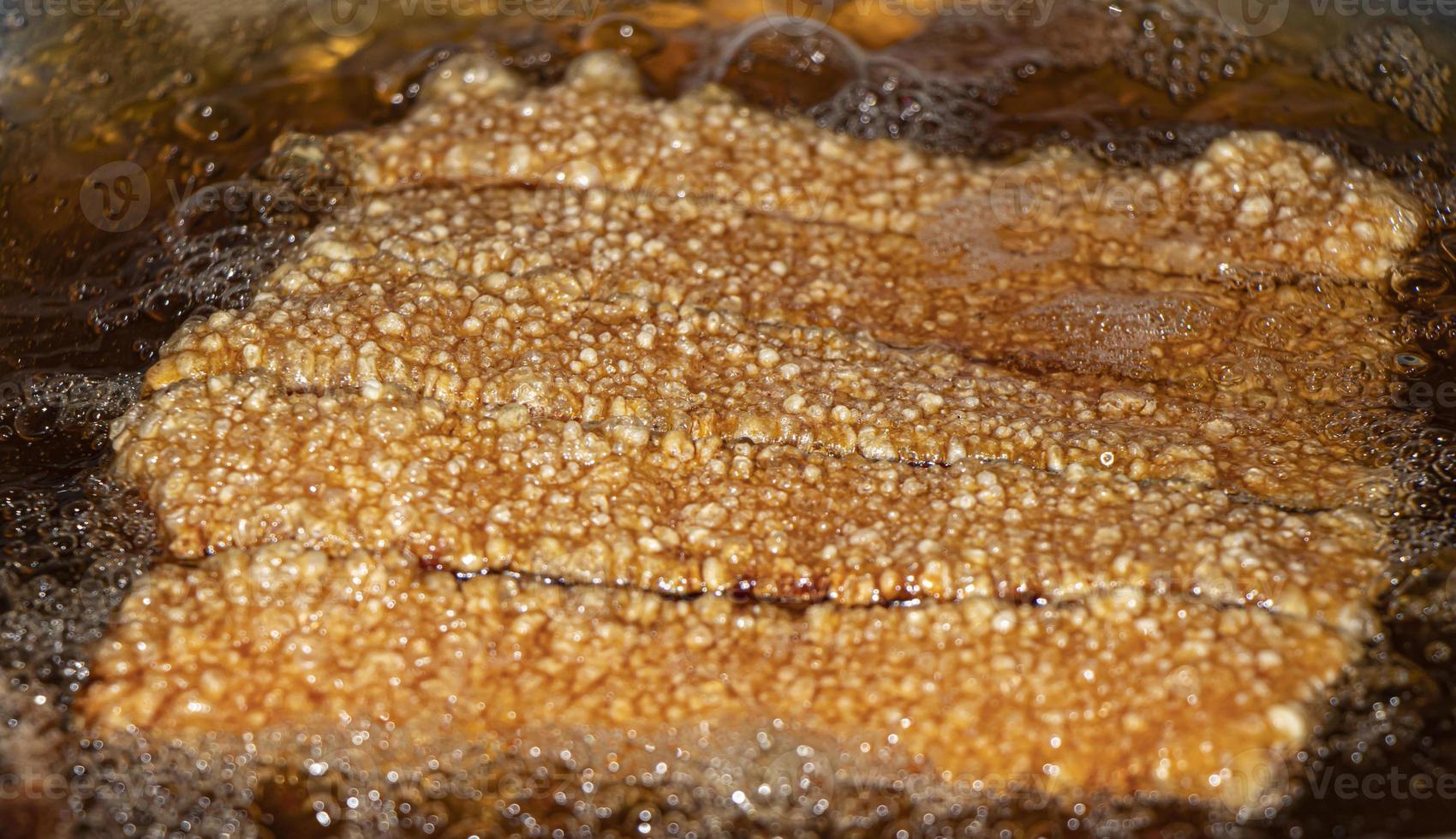 primo piano che frigge pancetta di maiale croccante su olio bollente. foto