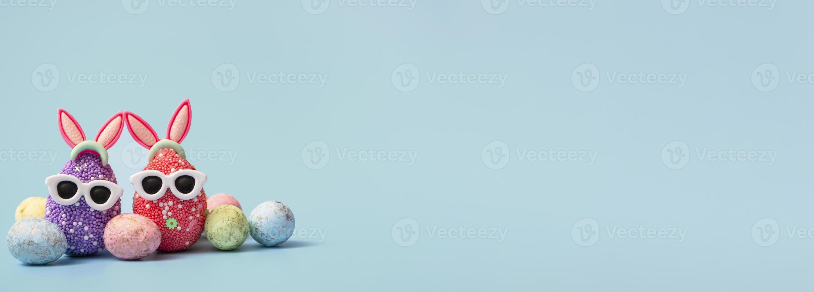 uovo di pasqua colorato con orecchie da coniglio e occhiali da sole su sfondo blu. banner di vendita, modello di mockup. copia spazio foto