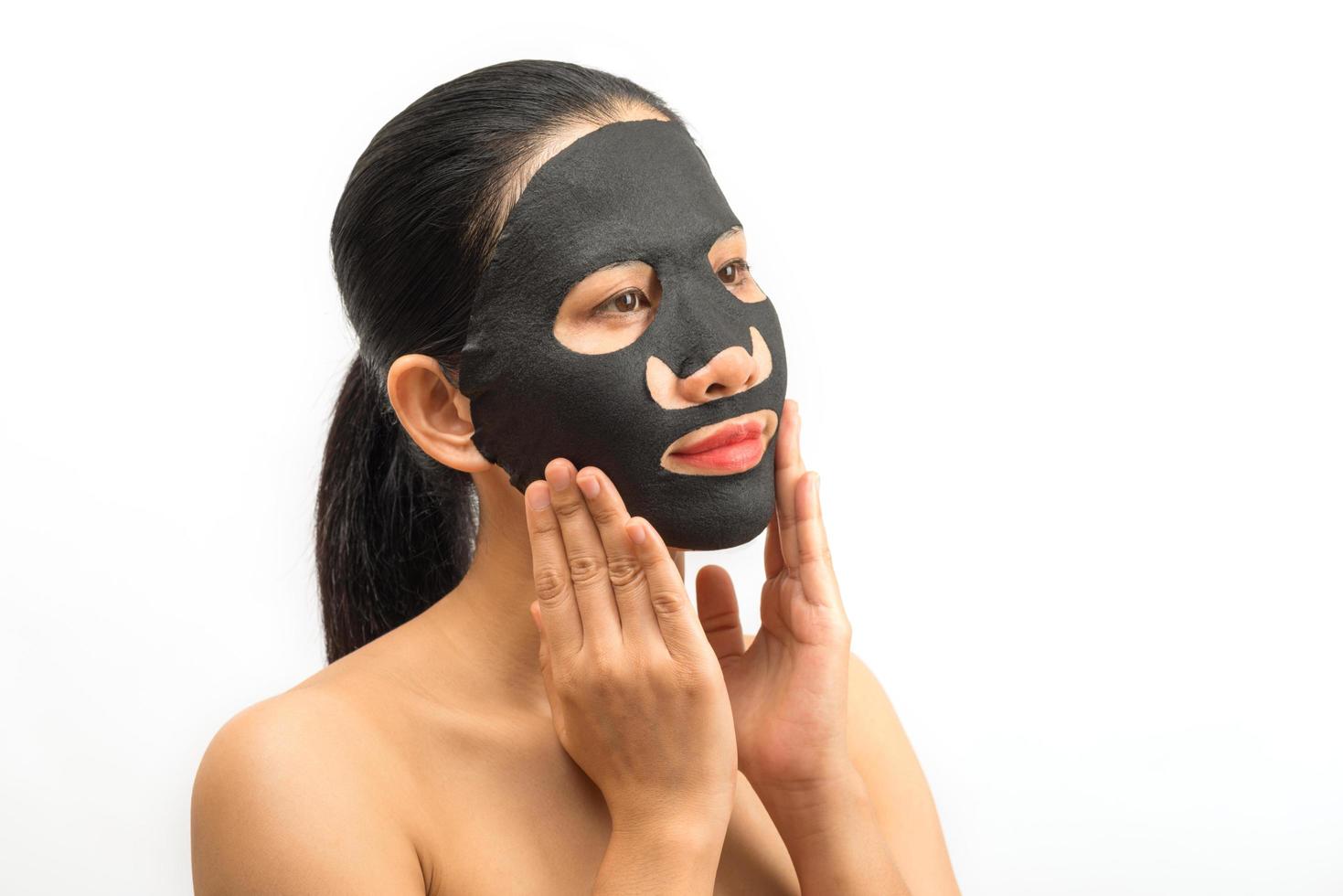 giovane donna che fa un foglio di maschera nera facciale con maschera purificante sul viso su sfondo bianco foto