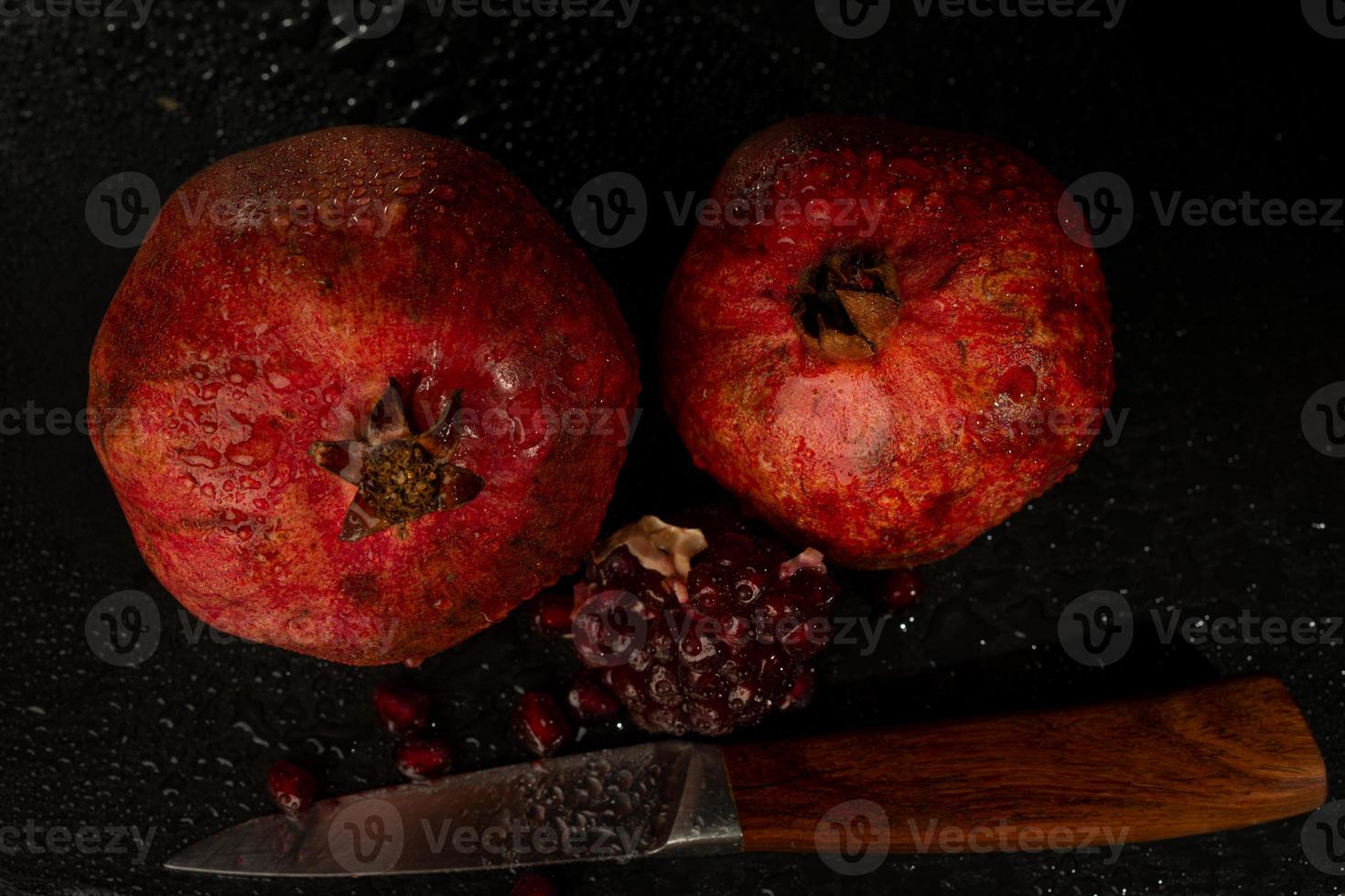 melograno bagnato maturo rosso su una tavola di pietra nera foto