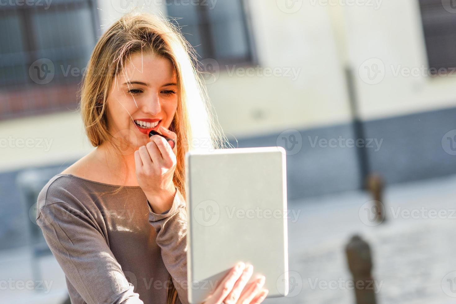 giovane donna che applica rossetto guardando tablet foto