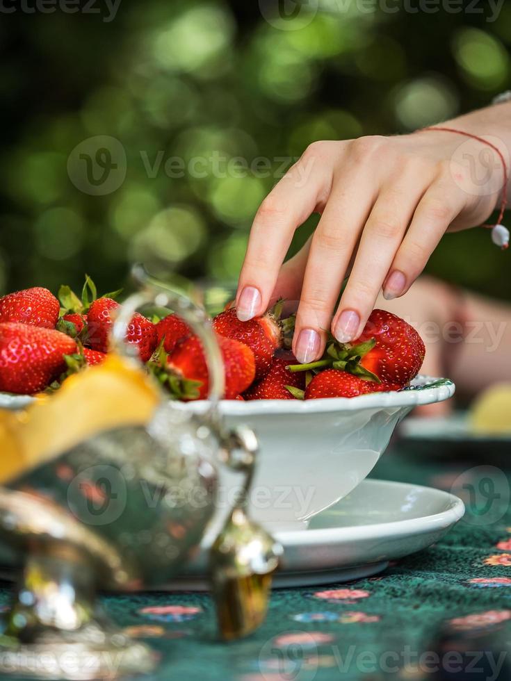 bella mano femminile con manicure prende una fragola da un piatto. tavola ben apparecchiata. dolce. luce del sole. giovinezza e freschezza. foto